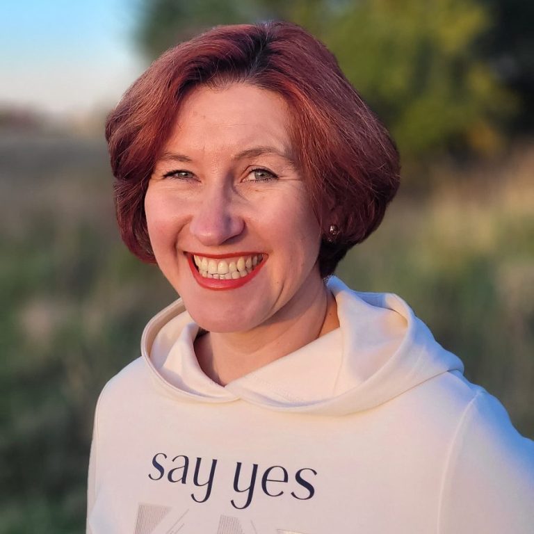 Porträt einer Frau mit kurzen Haaren und in heller Kleidung, lächelt in die Kamera